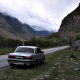 A large gray Volga car parked next to a road. The road passes through a rocky valley, the sky is very cloudy.