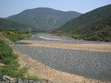 A large river bed of grey stones, with a comparatively thin river flowing.