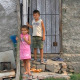 Two chilren stand in front of a poor house.