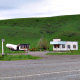 Beside a road, there is a green grass hill, with some cattle grazing.