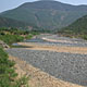 A large river bed of grey stones, with a comparatively thin river flowing.