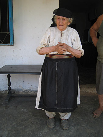 An old woman wearing a traditional white shirt with a long black skirt.