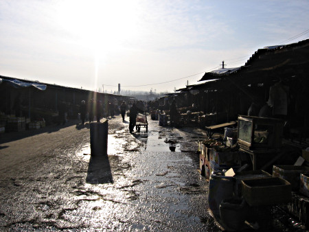 A high contrast picture of a market with boxes in show on both sides of a watery street.