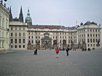 A square. Besides it, a large building with high entrance gates.