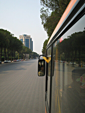 Picture taken from a bus showing a long boulevard without cars with trees at its side.