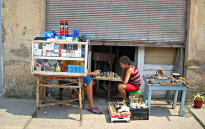 Two children playing chess beside boxes of cigarettes and other merchandise.