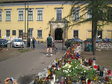 A yellow building; many candles on a little wall in front of it